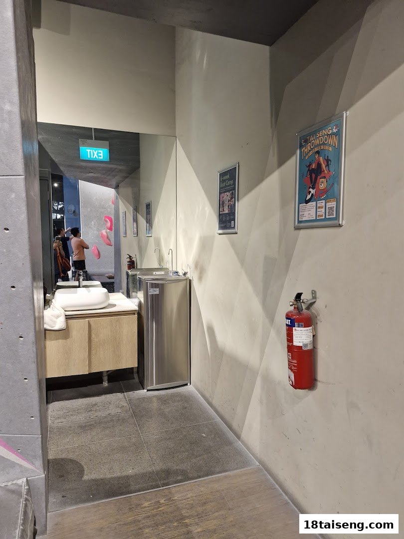 Interior view of Boulder Movement Tai Seng's washroom area with sink, water cooler, and posters, reflecting a climbing wall.