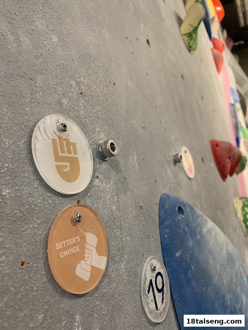 Close-up of a bouldering wall showing colorful climbing holds and route markers, including a 'SETTER'S CHOICE' tag.