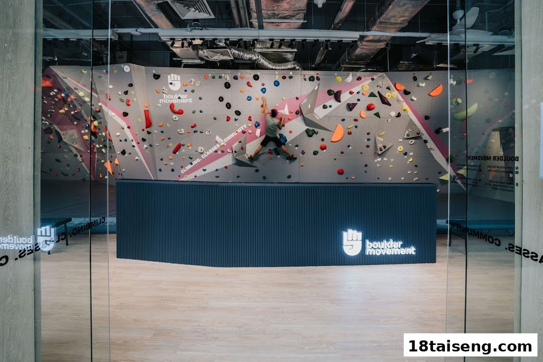 A person bouldering on a vibrant climbing wall inside Boulder Movement, viewed through a glass entrance.