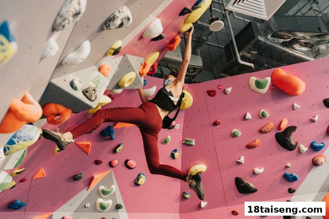 A person in athletic wear bouldering on a vibrant pink and grey climbing wall with colorful holds.