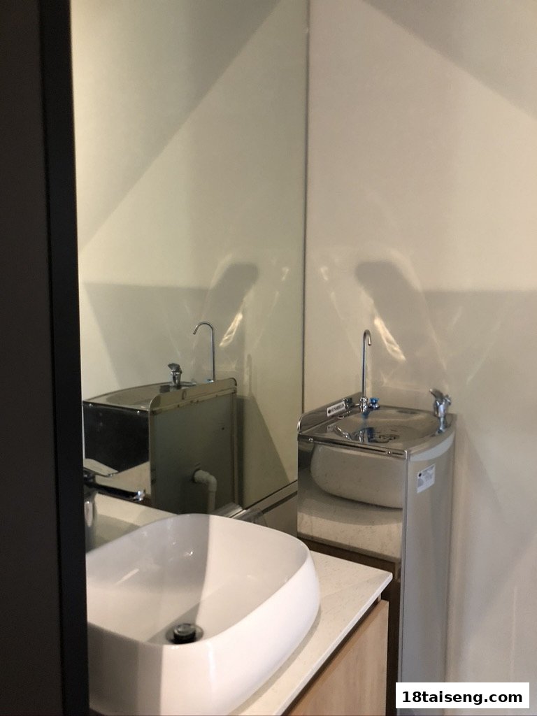 A clean restroom area featuring a modern sink and a water dispenser, reflecting in a mirror.