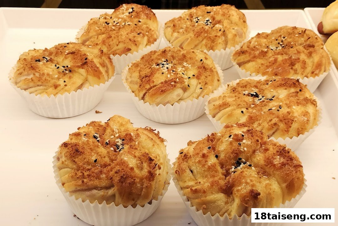 A tray of golden-brown baked buns, topped with savory floss and sesame seeds, displayed in white paper cups.