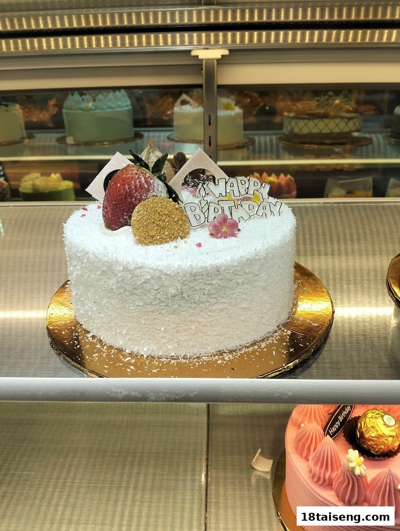 A white birthday cake with strawberry and 'Happy Birthday' topper in a bakery display case.