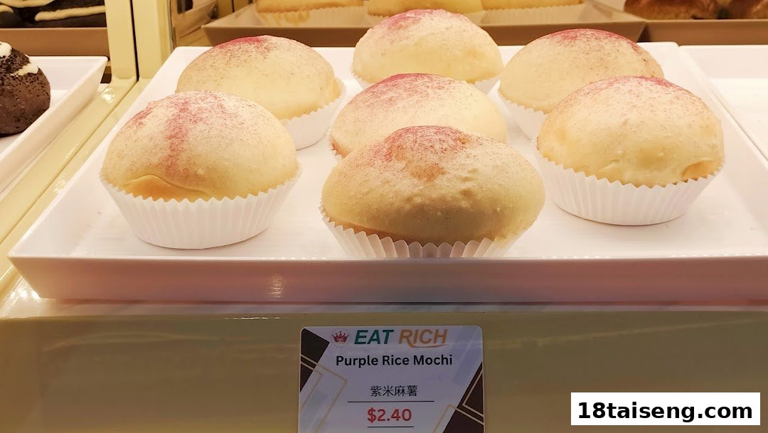 A display of several light-colored mochi buns with a purple dusting, presented in white paper cups.