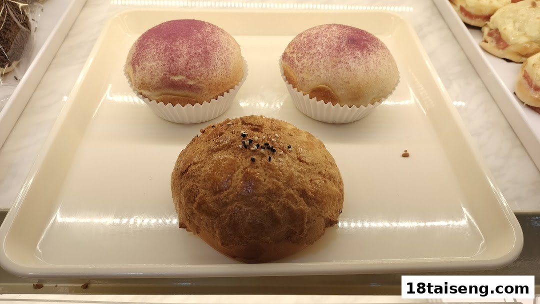 A display of freshly baked buns, including two purple-dusted pastries and a sesame-topped bun.