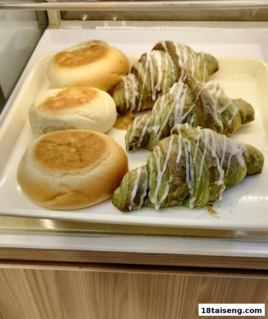 A display of freshly baked goods, including round buns and green croissants with white icing.