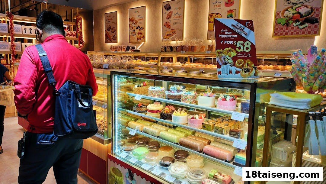 A customer views a vibrant display of cakes and pastries inside a bustling bakery.