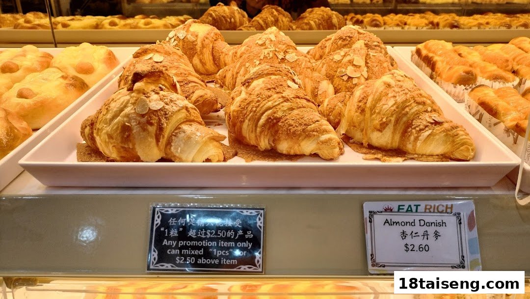 A display case filled with golden almond croissants and other pastries, featuring price tags and a promotion.