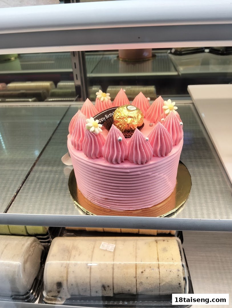 A vibrant pink birthday cake with a Ferrero Rocher and other pastries displayed in a bakery case.