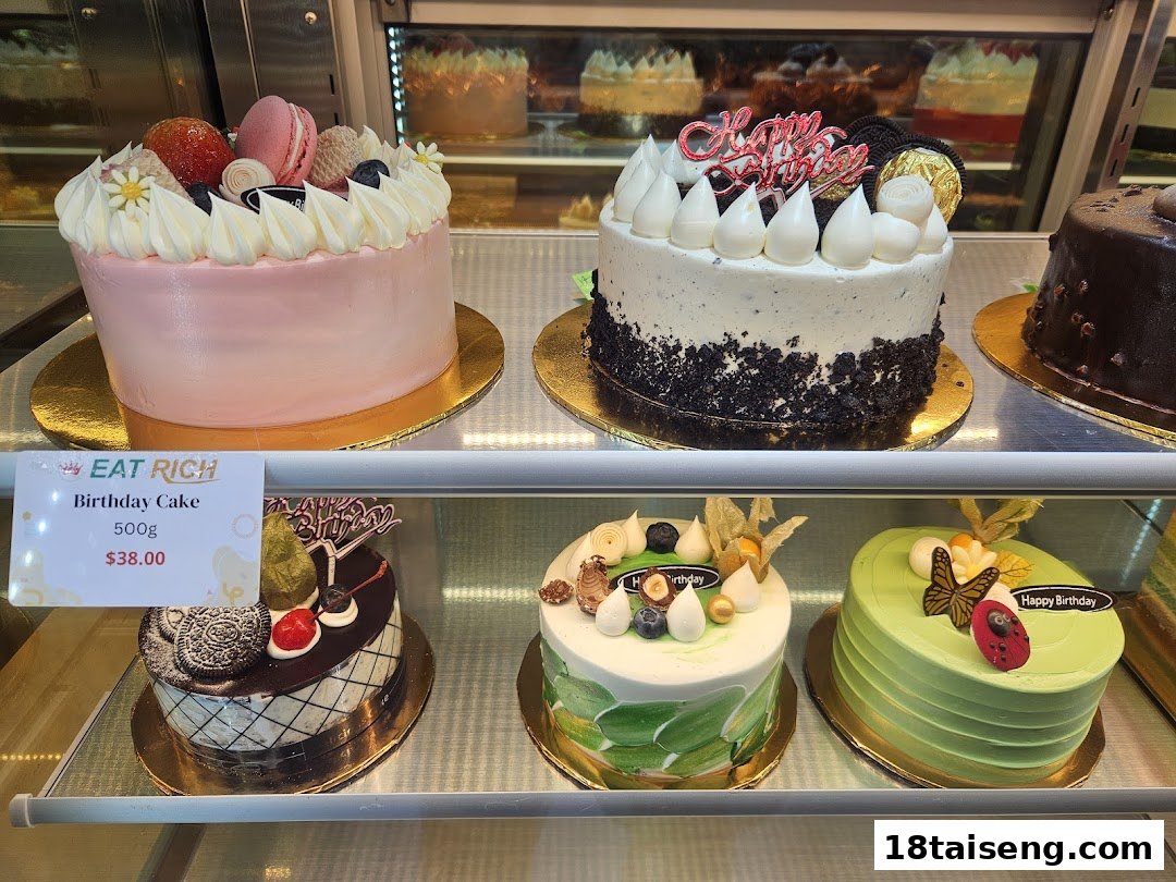 A vibrant display of beautifully decorated birthday cakes in a glass showcase at Eat Rich.