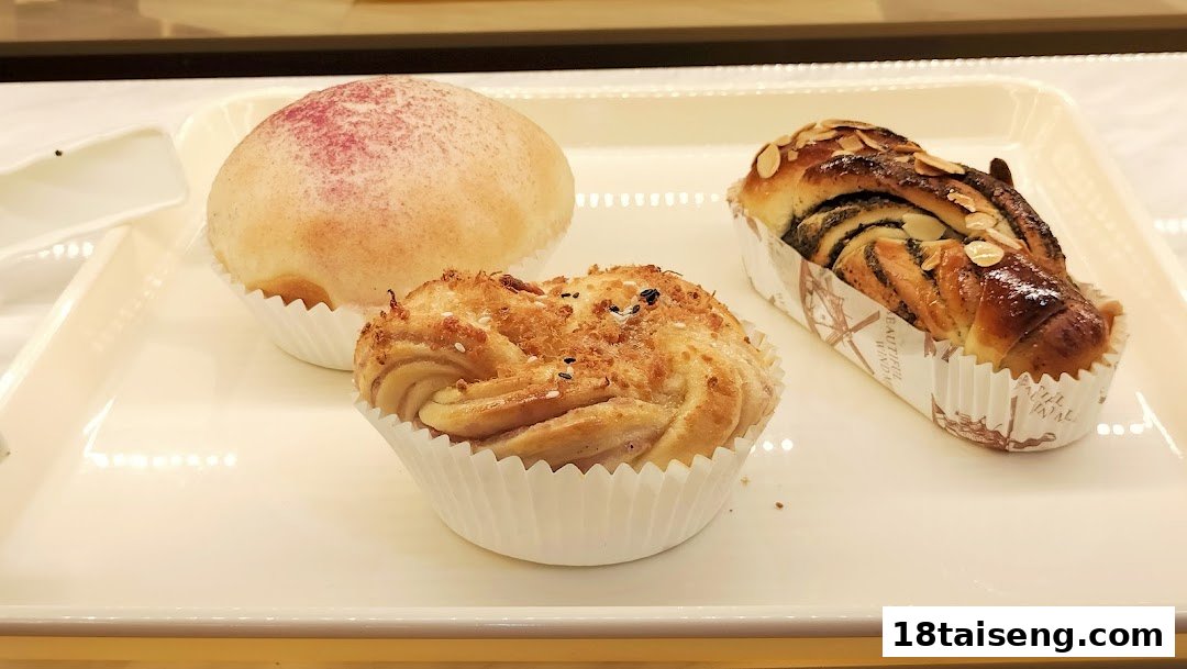 A white tray showcases three delicious baked goods: a bun, a savory pastry, and a braided loaf.