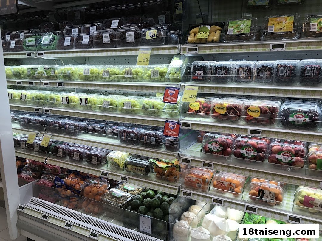 A well-stocked refrigerated display of fresh, pre-packaged fruits like grapes, berries, and stone fruits at FairPrice Tai Seng.