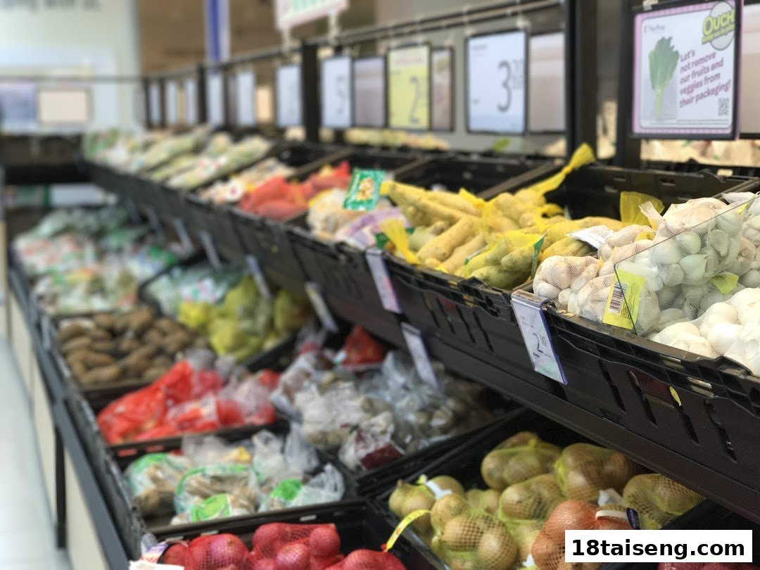 A well-stocked supermarket aisle displaying a variety of fresh fruits and vegetables in mesh bags and crates.