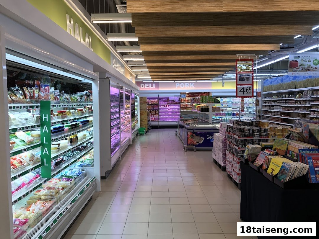 A wide aisle inside FairPrice Tai Seng supermarket, featuring refrigerated sections for Halal and Deli products.
