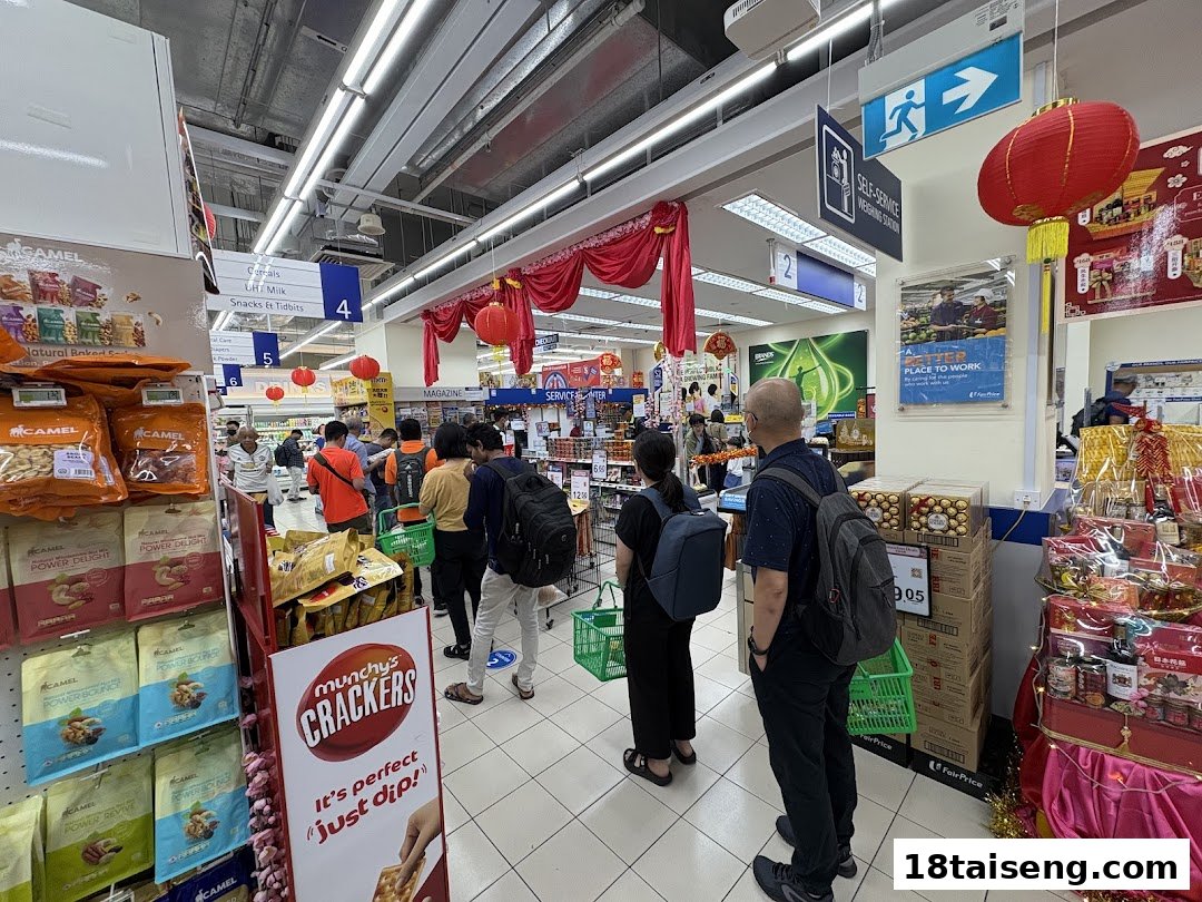 Customers browse aisles and queue at checkout in a well-stocked FairPrice supermarket, featuring snacks and festive decorations.