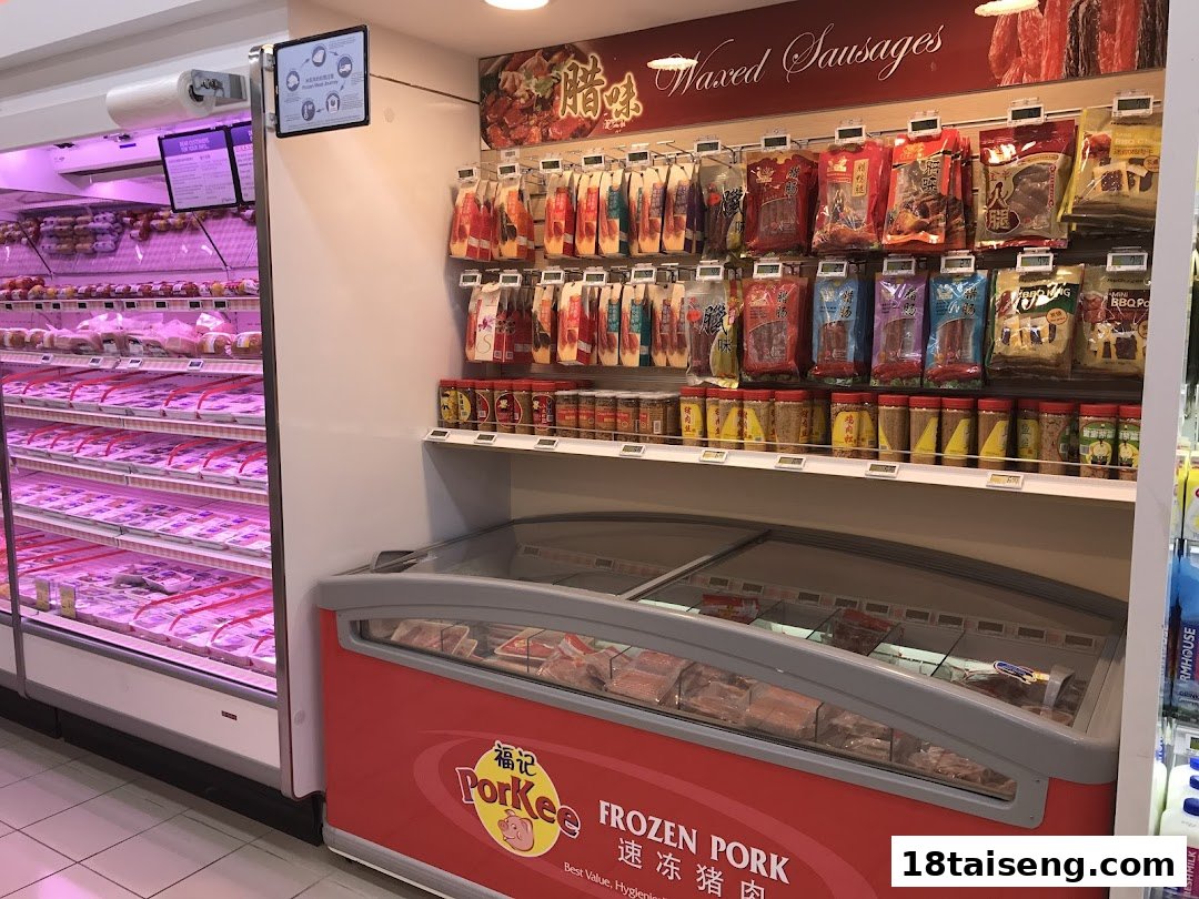 An interior view of FairPrice Tai Seng, showcasing refrigerated meat products and a display of packaged sausages.