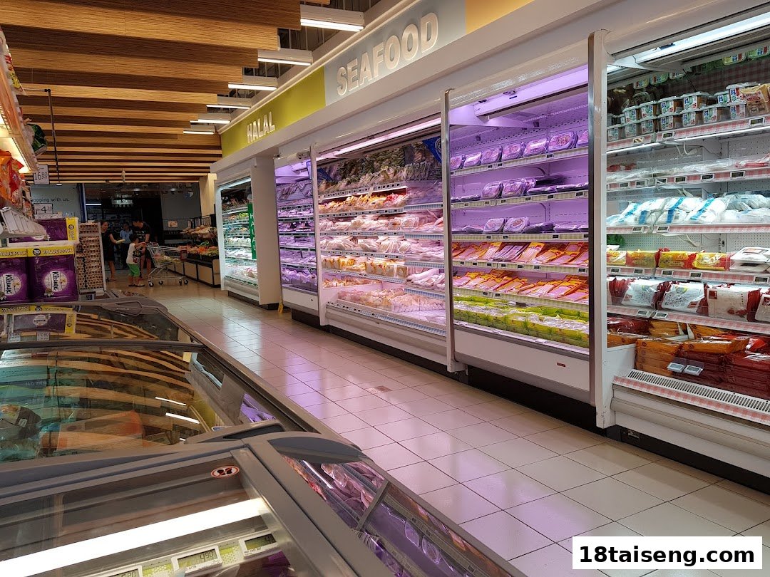 A well-stocked supermarket aisle featuring refrigerated sections for fresh seafood and halal products, with shoppers in the background.