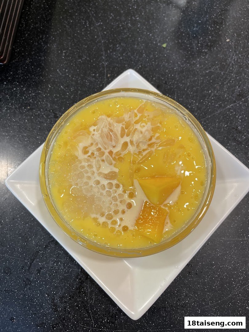 A vibrant bowl of mango sago dessert with fresh mango chunks and pomelo on a white plate.