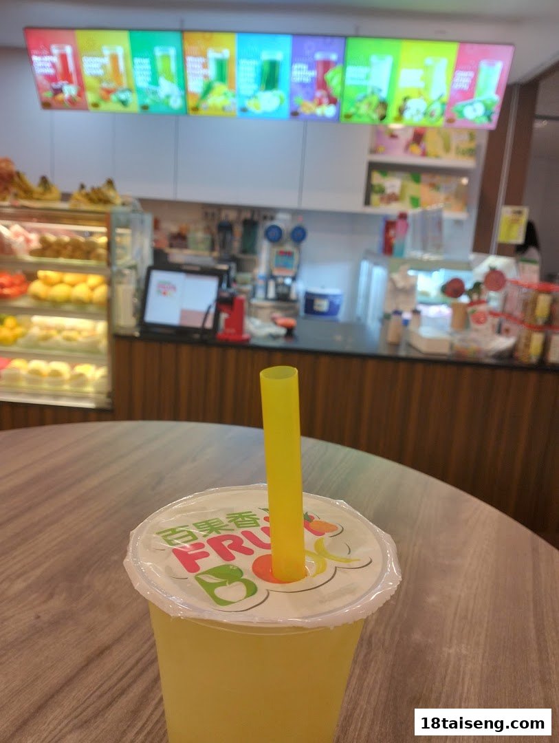 A refreshing fruit juice drink with a yellow straw on a wooden table, with the shop counter and menu boards in the background.