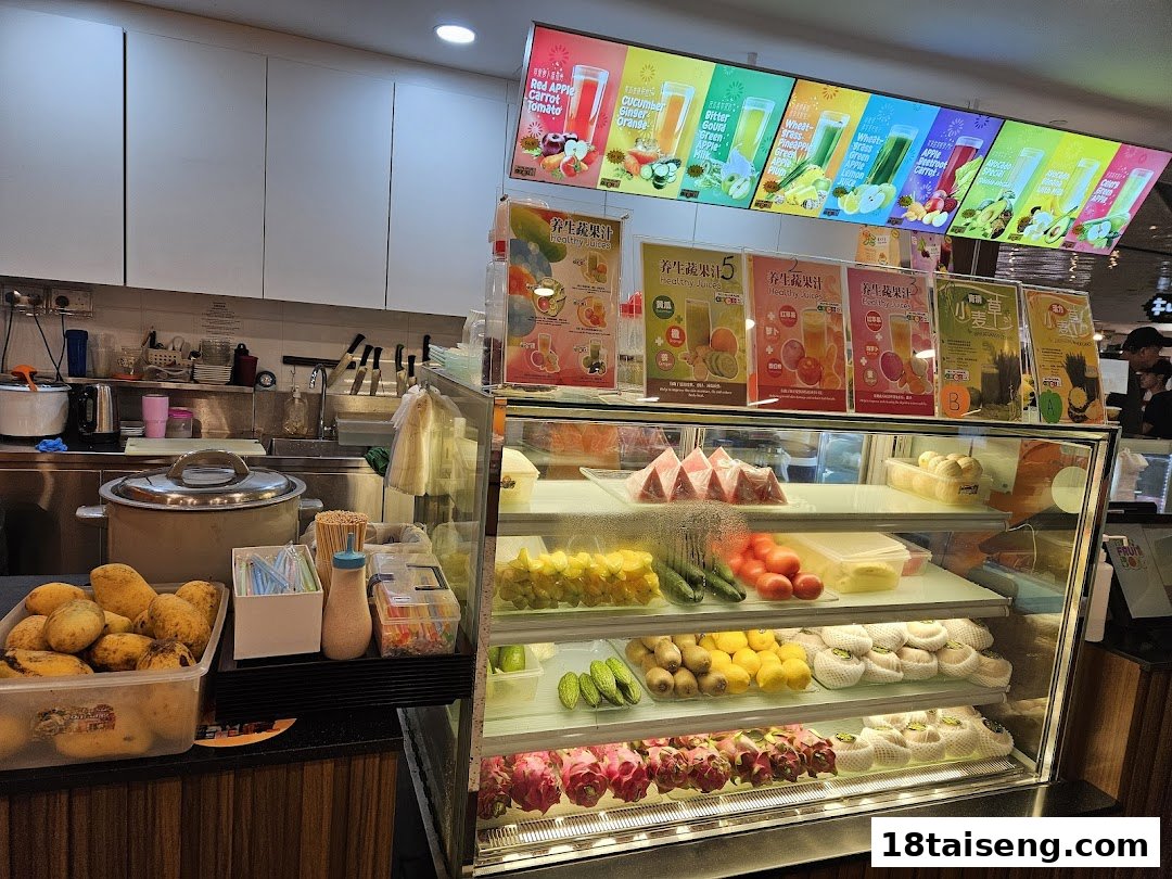 Interior view of a fruit juice shop showcasing fresh produce, display fridge, and vibrant menu boards.