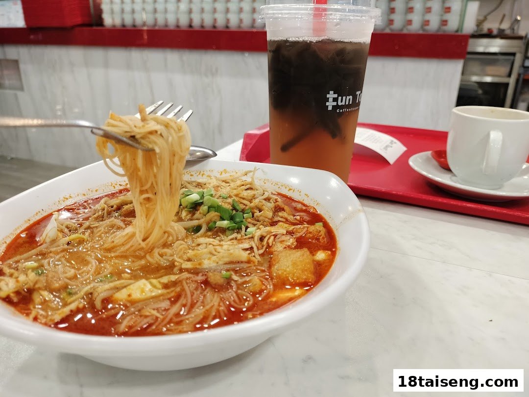 A close-up of a bowl of laksa noodles with a drink and coffee on a red tray.