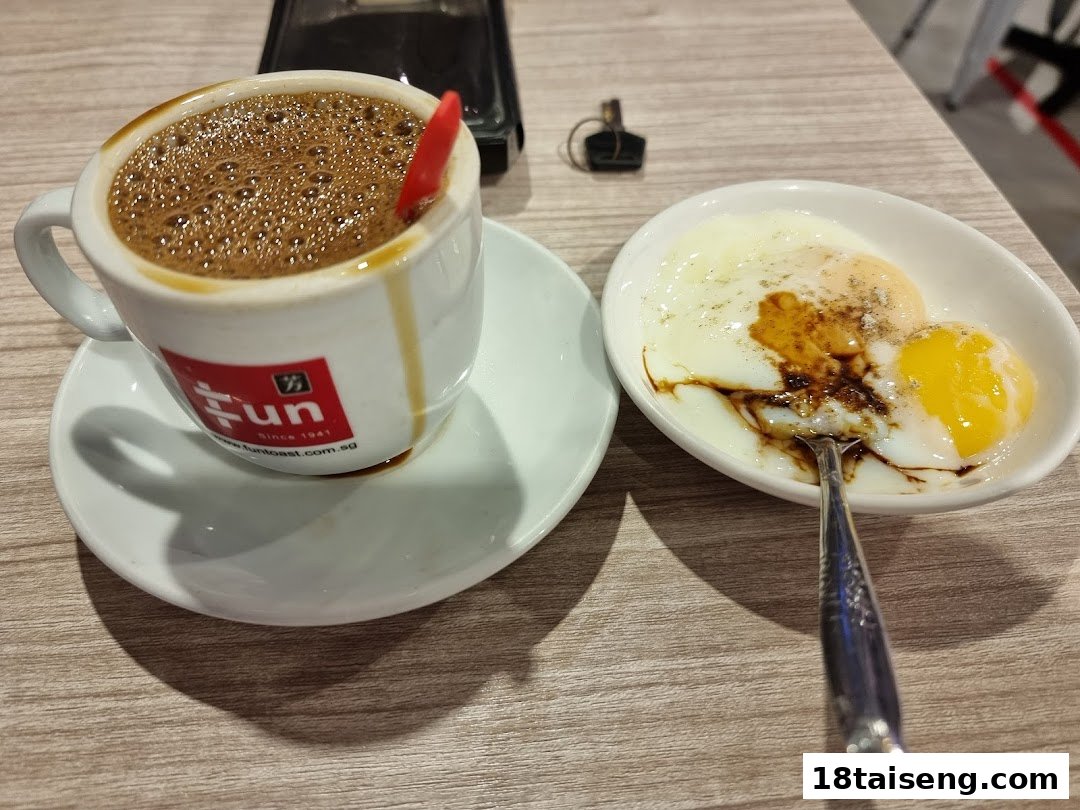 A cup of traditional kopi and soft-boiled eggs with soy sauce and pepper on a wooden table.