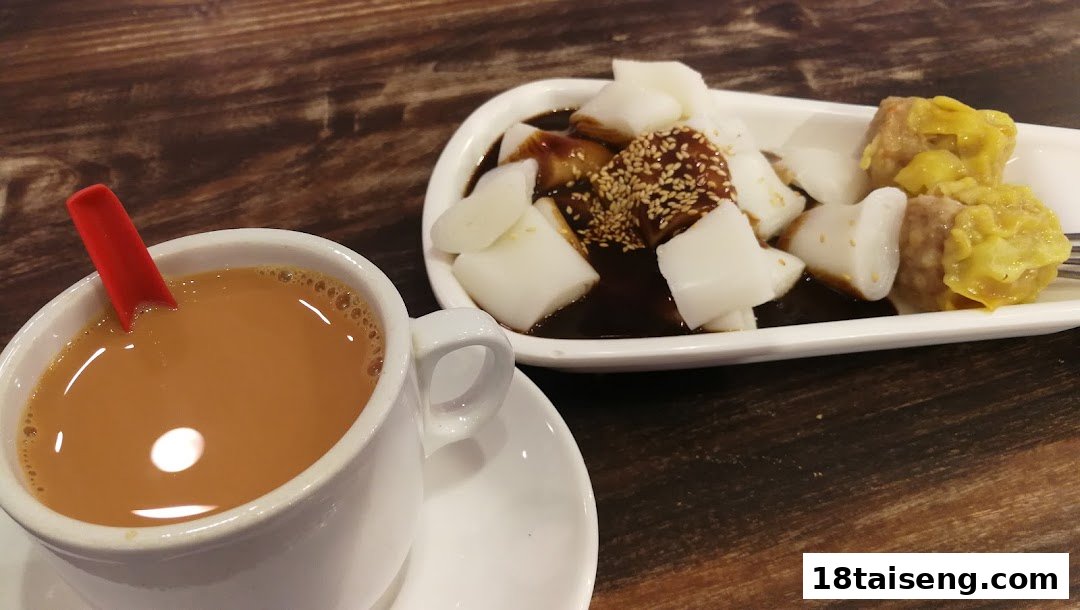 A cup of traditional coffee or tea with a plate of chee cheong fun and siew mai on a wooden table.