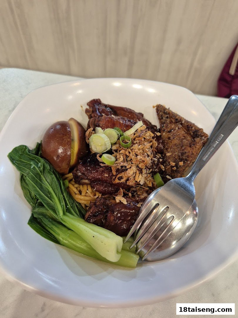 A close-up of a delicious noodle dish with braised meat, a soy-marinated egg, and green vegetables.