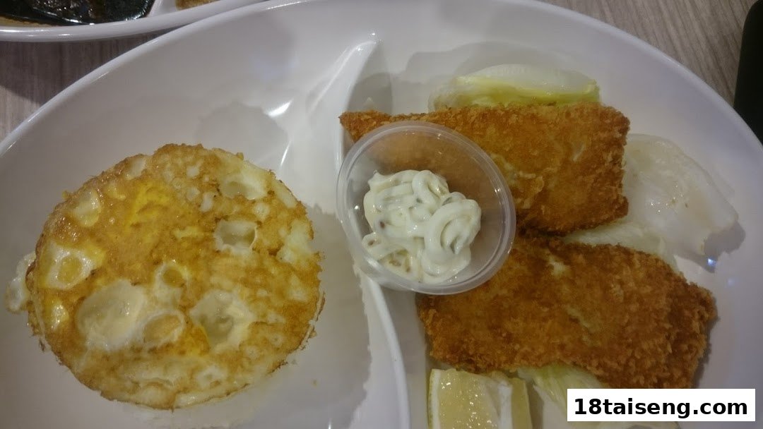 A close-up of a meal featuring crispy fried fish fillets, a sunny-side-up egg, and tartar sauce.