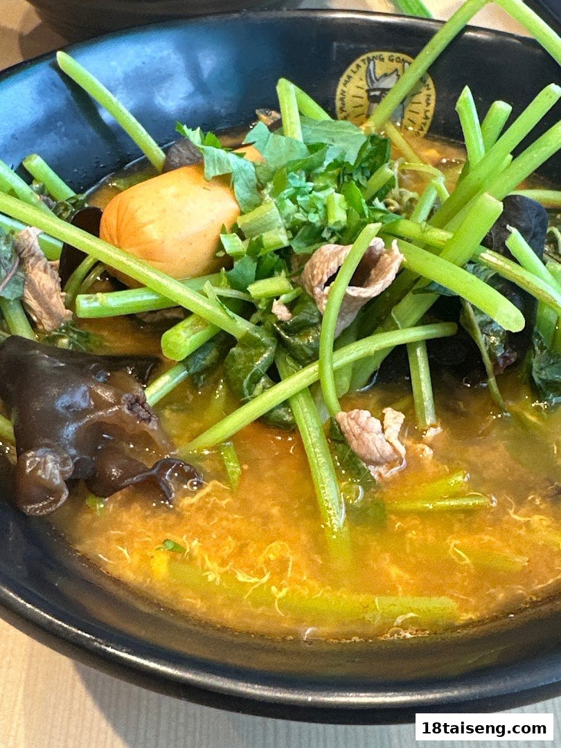 A close-up of a vibrant bowl of Malatang with vegetables, meat, and a sausage in a rich broth.