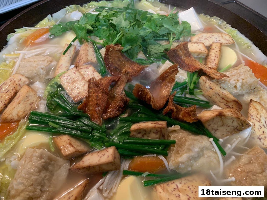 A close-up of a bubbling hotpot with fresh vegetables, taro, fish cakes, and various ingredients.