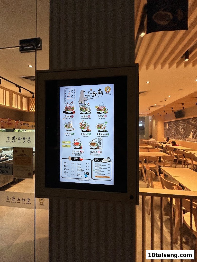 A digital menu display at the entrance of Gong Yuan Ma La Tang, showcasing various soup bases, add-ons, beverages, and dumplings.
