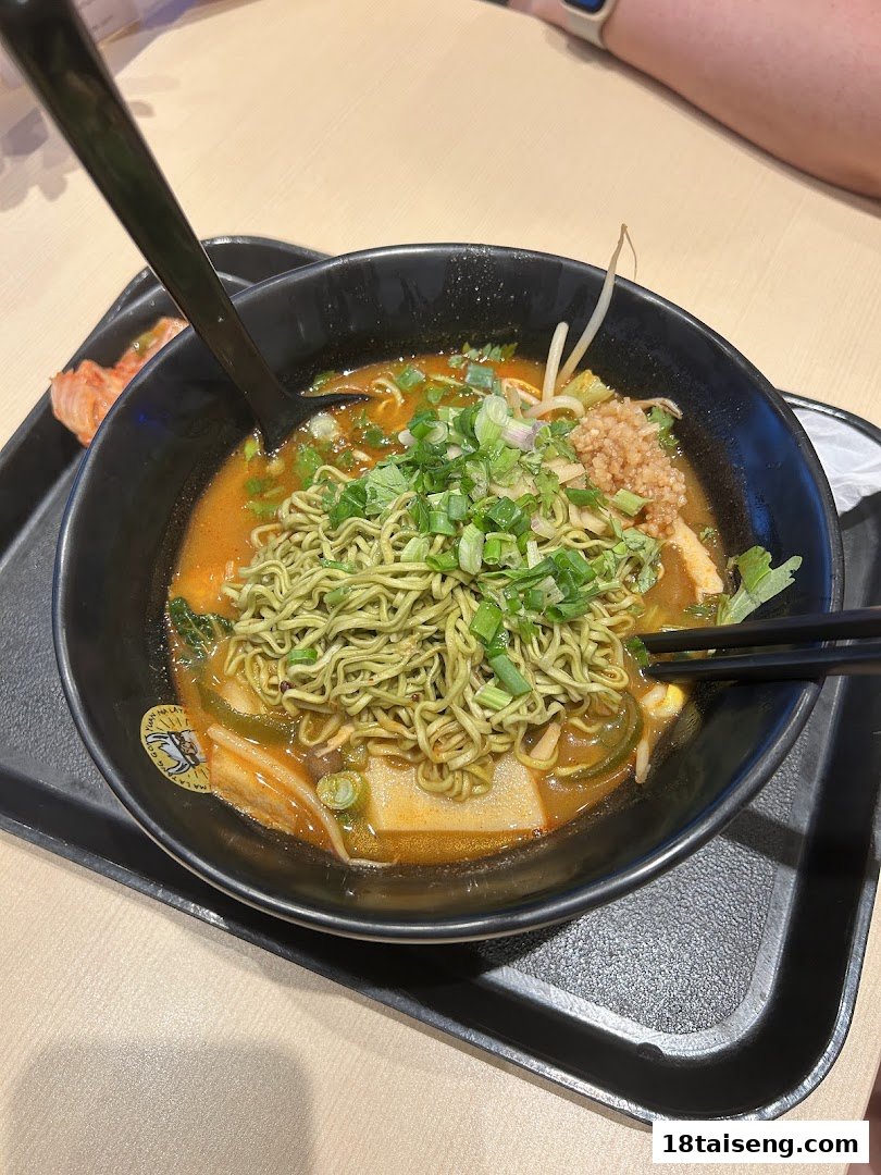 A vibrant bowl of green noodles with broth and various toppings, served on a black tray.