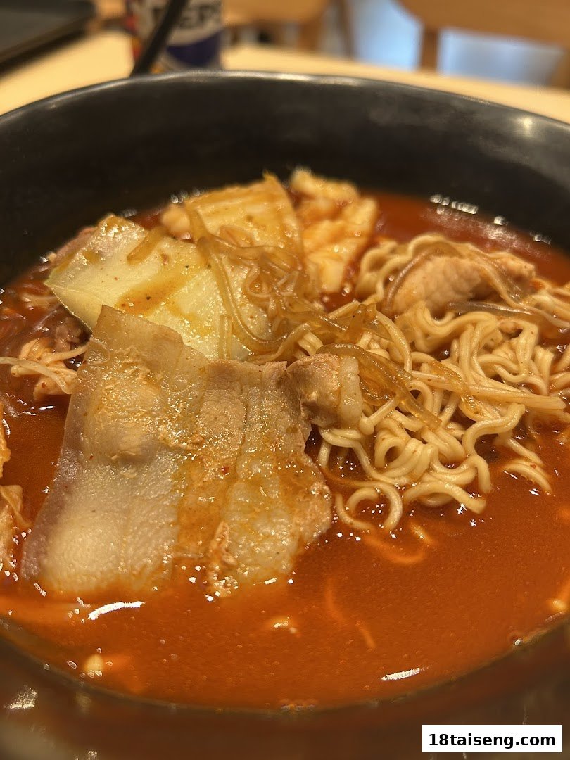 A close-up of a vibrant bowl of spicy noodles with pork belly, cabbage, and glass noodles.
