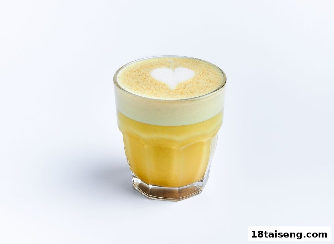 A vibrant yellow latte with a heart-shaped latte art in a clear glass.
