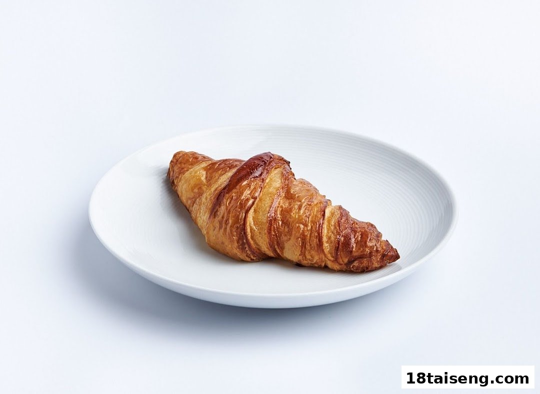 A golden-brown croissant rests on a white plate against a clean background.