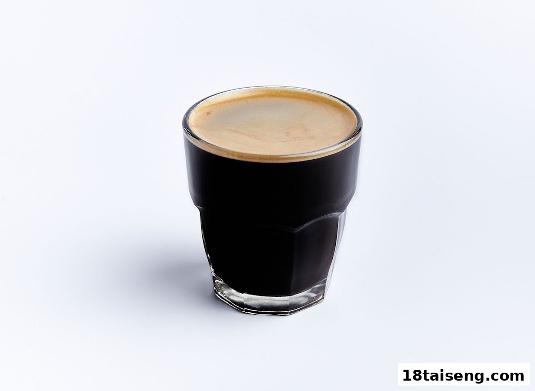 A glass of dark coffee with a layer of light brown crema on a white background.