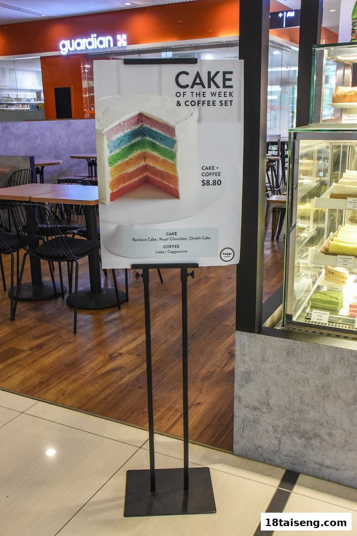 A promotional sign for Huggs Coffee's 'Cake of the Week & Coffee Set' featuring a rainbow cake.