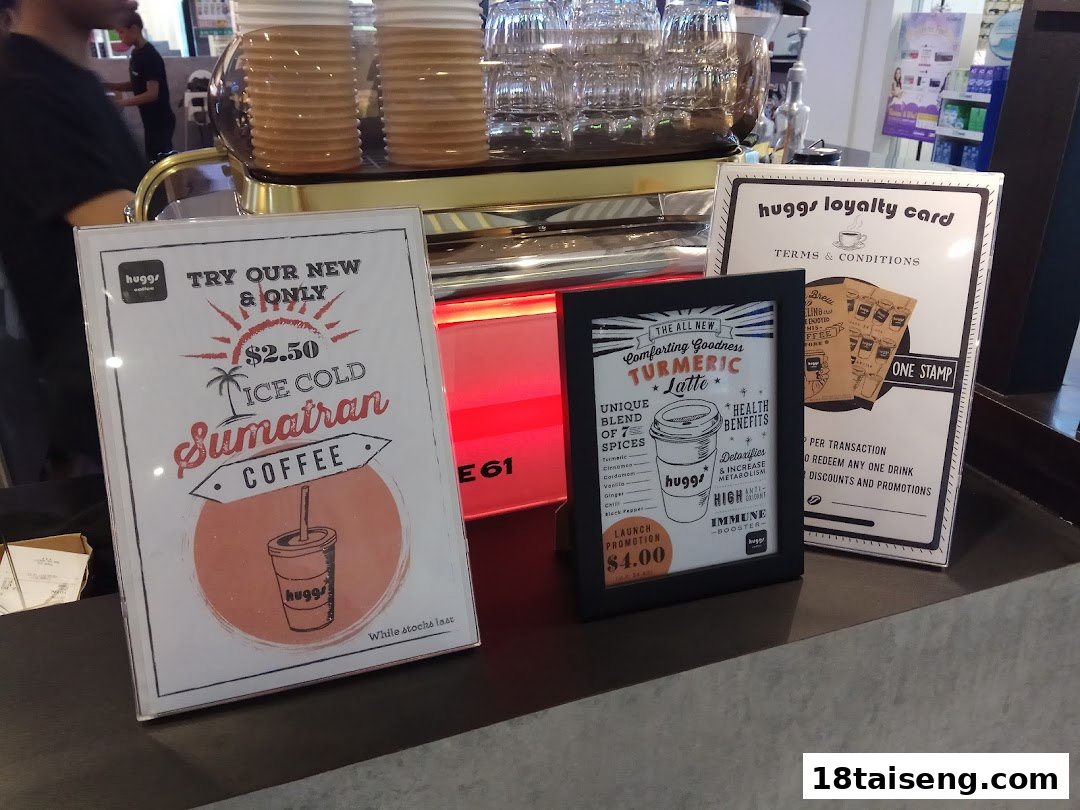 Promotional signs for coffee and turmeric latte, plus a loyalty card, displayed at Huggs Coffee counter.