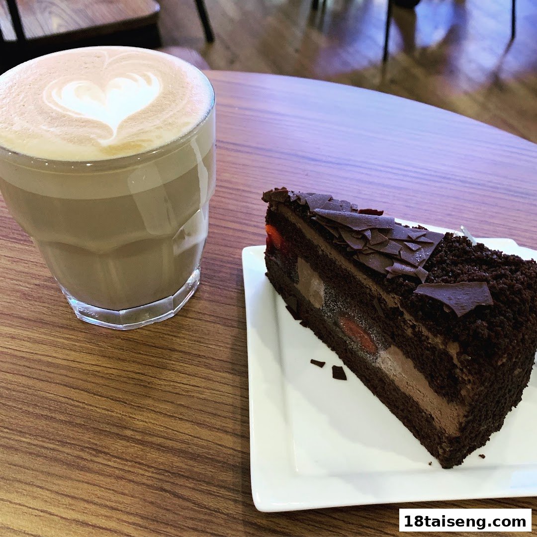 A heart-latte art coffee and a slice of chocolate cake on a wooden table.