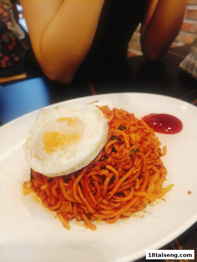 A vibrant plate of spicy noodles topped with a perfectly fried egg and a dollop of sauce.