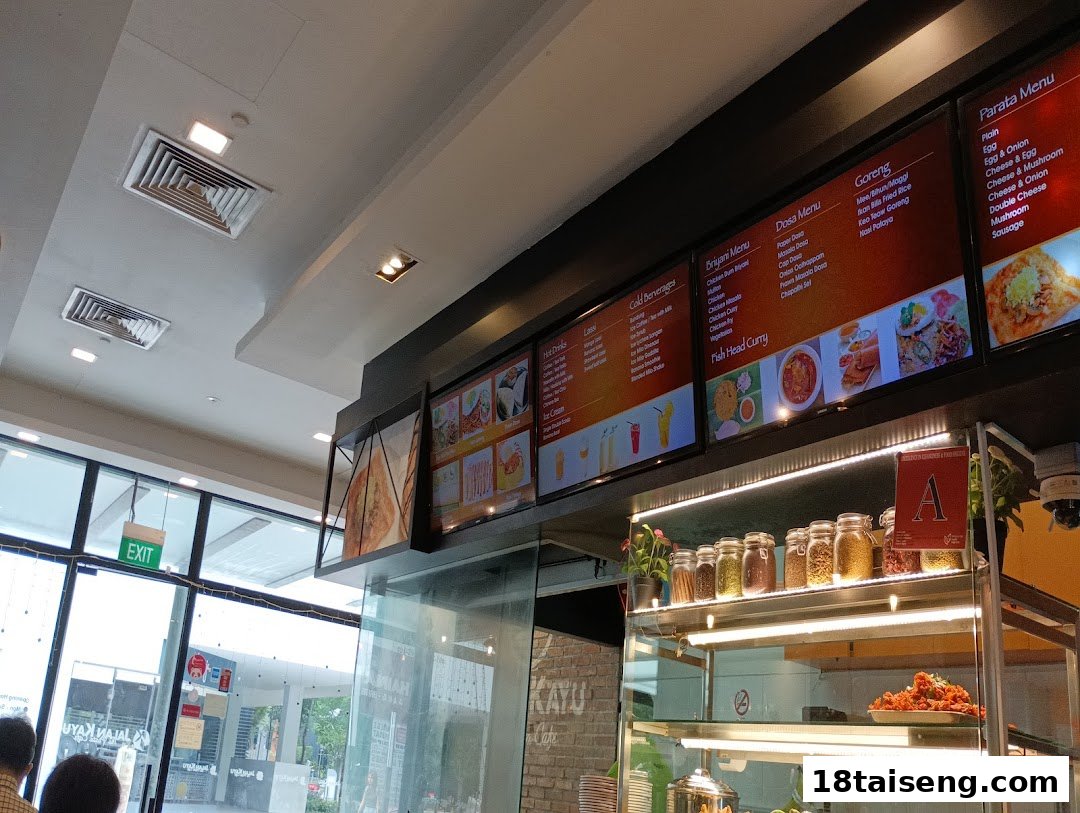 Interior view of Jalan Kayu The Prata Cafe, showing digital menu boards and a food display.