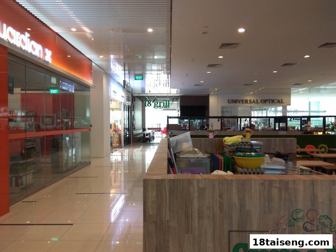 Interior view of a modern mall corridor with diverse shops and a food preparation counter in the foreground.
