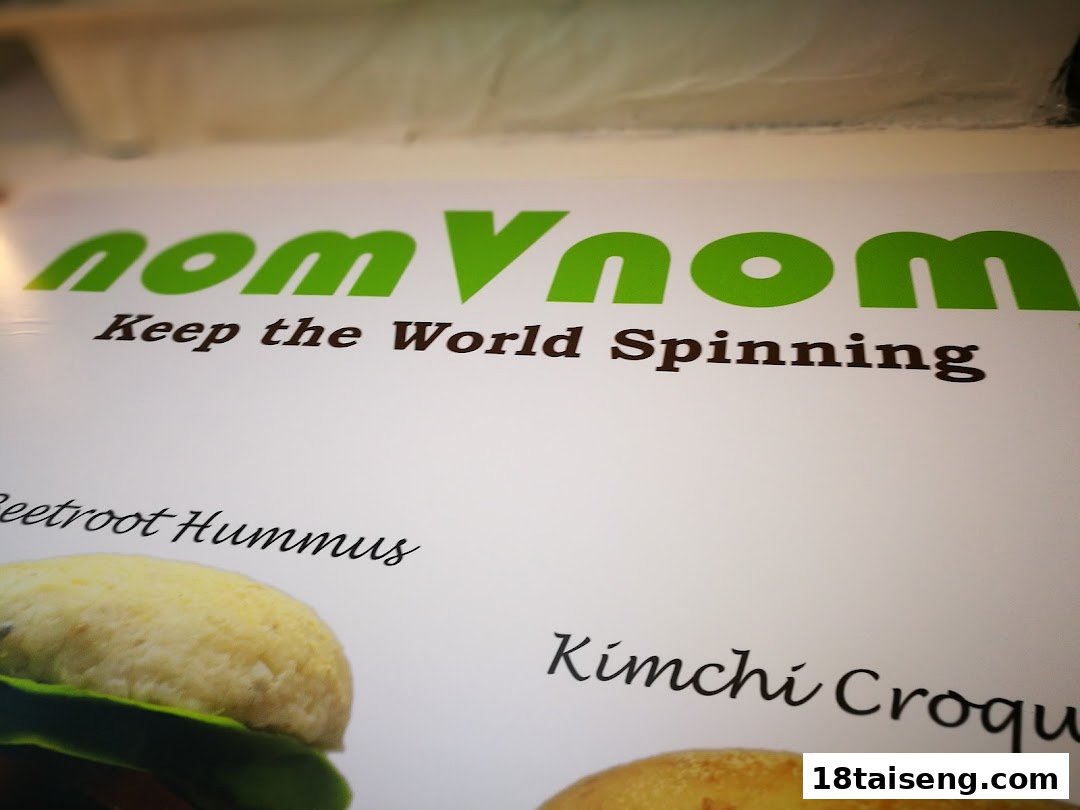 A close-up of a nomVnom sign featuring their logo, tagline, and partial views of plant-based food items.