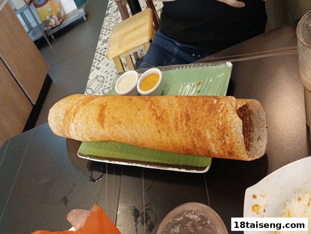 A golden-brown dosa served on a green plate with two dipping sauces at a cafe.