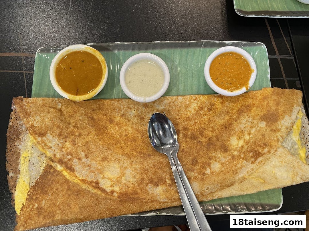 A golden-brown dosa served with three vibrant chutneys on a green banana leaf-patterned plate.