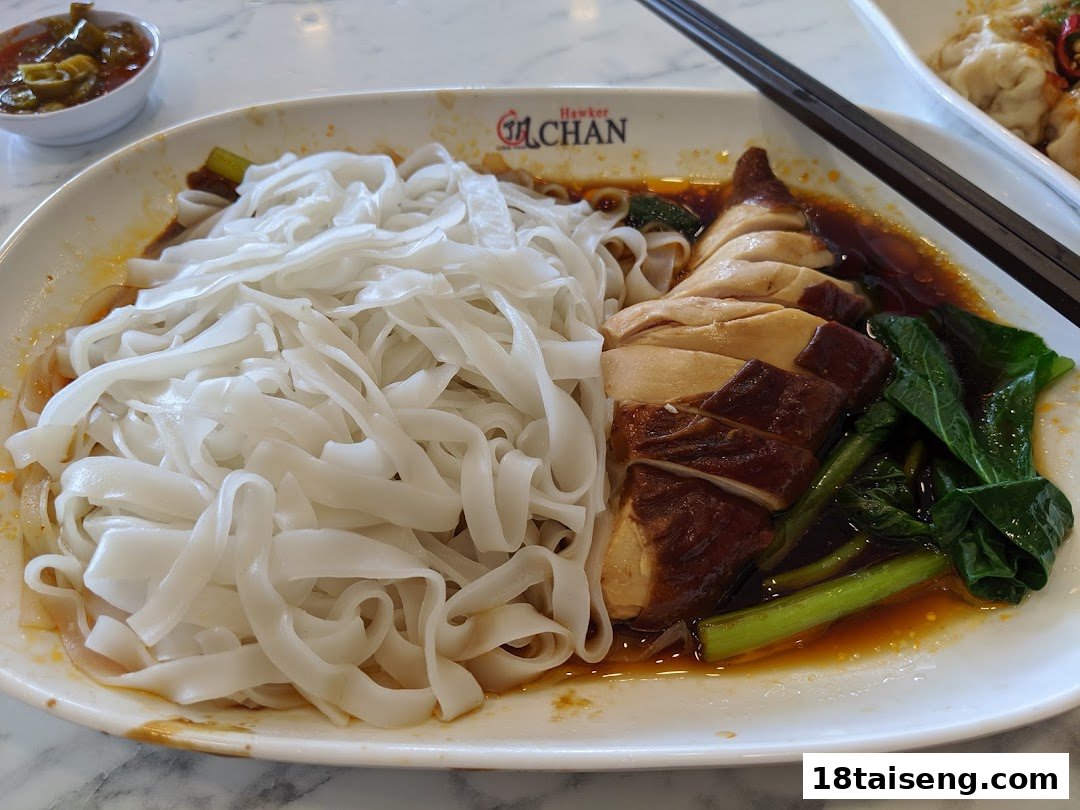 A delicious plate of flat rice noodles with soy sauce chicken and green vegetables.