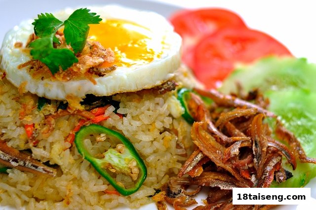 A close-up of delicious fried rice topped with a sunny-side-up egg, crispy anchovies, and fresh vegetables.