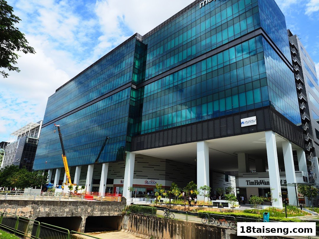 A modern glass-facade building housing various retail shops at ground level, beside a canal.