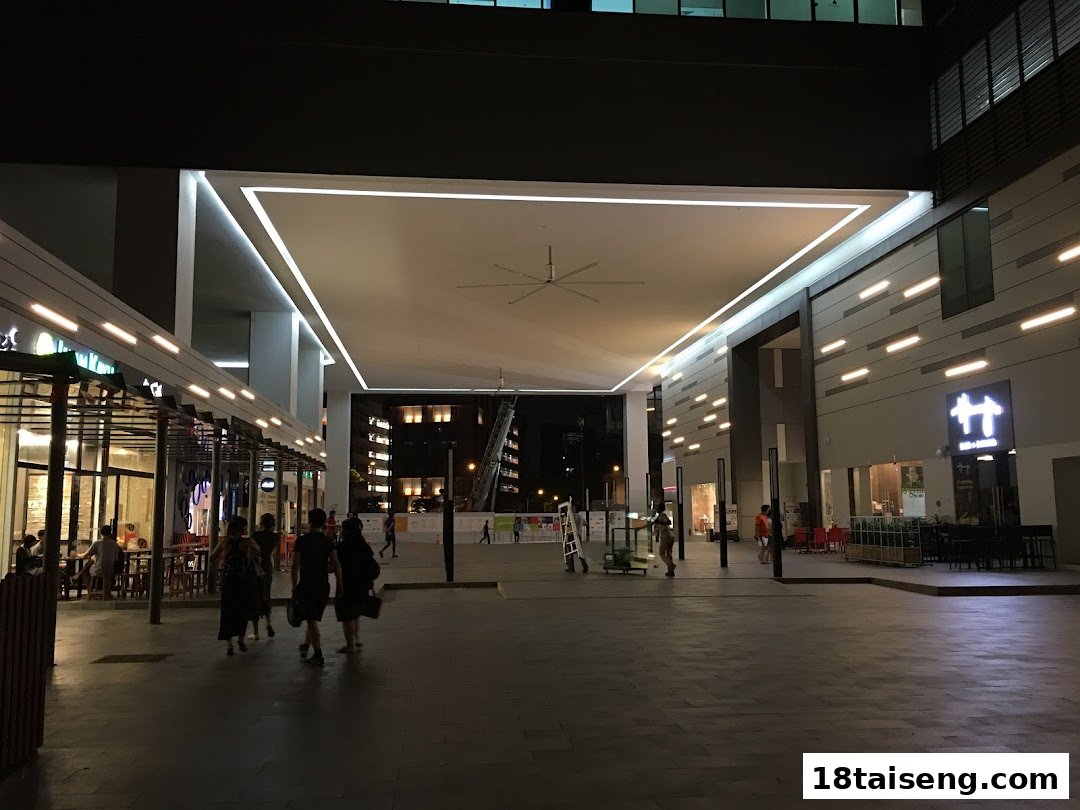 An evening view of an outdoor mall area with shops, people walking, and illuminated architecture.